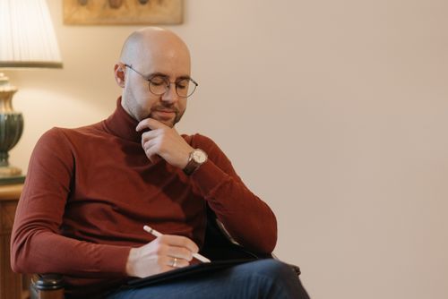Free Bald man with eyeglasses writing with a digital pen in a cozy indoor setting. Stock Photo