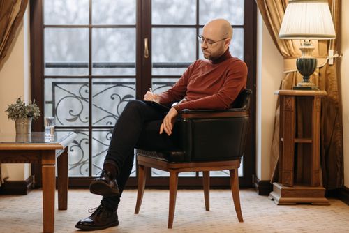 Free Bald man in armchair writing notes beside window in cozy room. Stock Photo