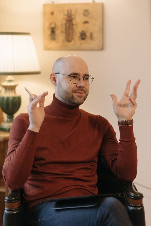 Free Man in red turtleneck gesturing while speaking indoors with artful decor. Stock Photo