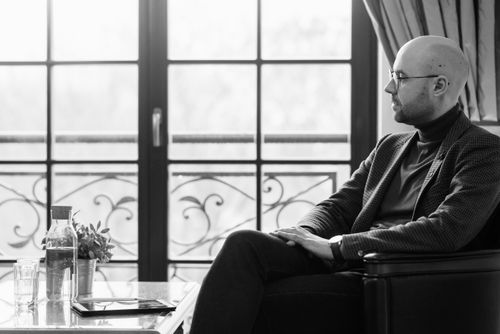 Free Black and white portrait of a bald man sitting thoughtfully near a window indoors. Stock Photo