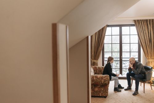 Free Two professionals in a serious discussion in a tastefully decorated office, featuring cozy furniture and large windows. Stock Photo