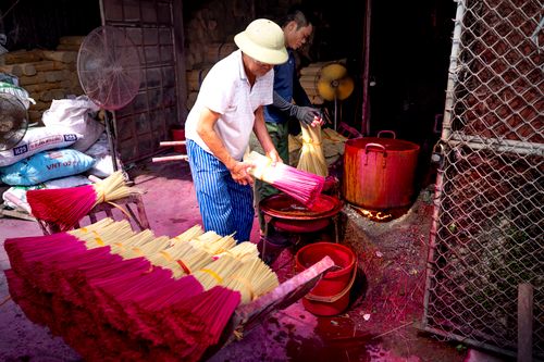 Free Ethnic workers in casual clothes coloring bundles of incense bamboo sticks in red pigment working on local manufacture in daytime Stock Photo