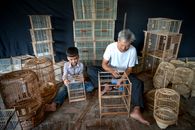 From above of gray haired male master and boy sitting on floor while weaving cages in workshop