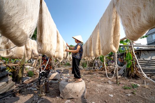 Side view of anonymous Asian artisan checking and collecting fibres of silk threads hanging on bamboo sticks to dry in sun in village in summer