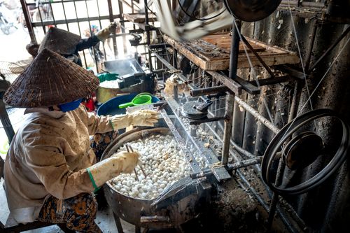 Free Side view of concentrated anonymous artisans in hats boiling water with cocoons of silk warms and weaving threads while working on factory Stock Photo