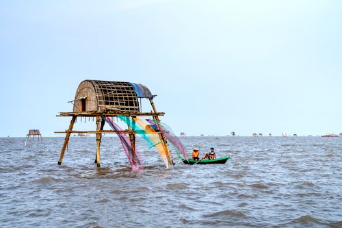 Free Fishermen of Vietnamese people in boat moored near wooden hut on stilts in waters of ocean off coast in daylight Stock Photo