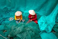 Unrecognizable women in Vietnamese hats repairing fishing nets