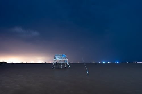 Scenic view of lifeguard tower on sandy shore with lights under cloudy sky at sunset