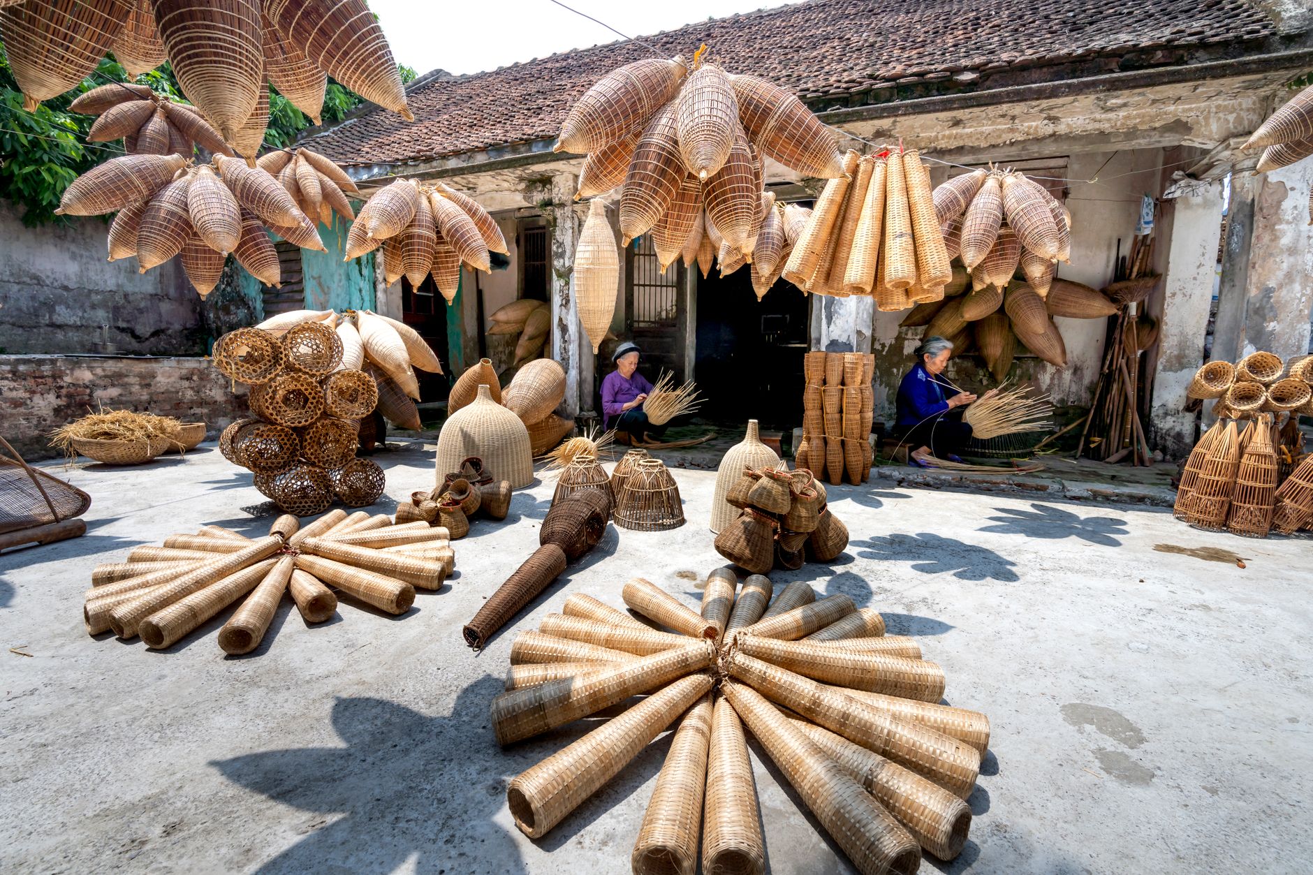 Collection of wooden fish traps hanging on ropes and placed on gray ground near weathered house and ethnic people workin