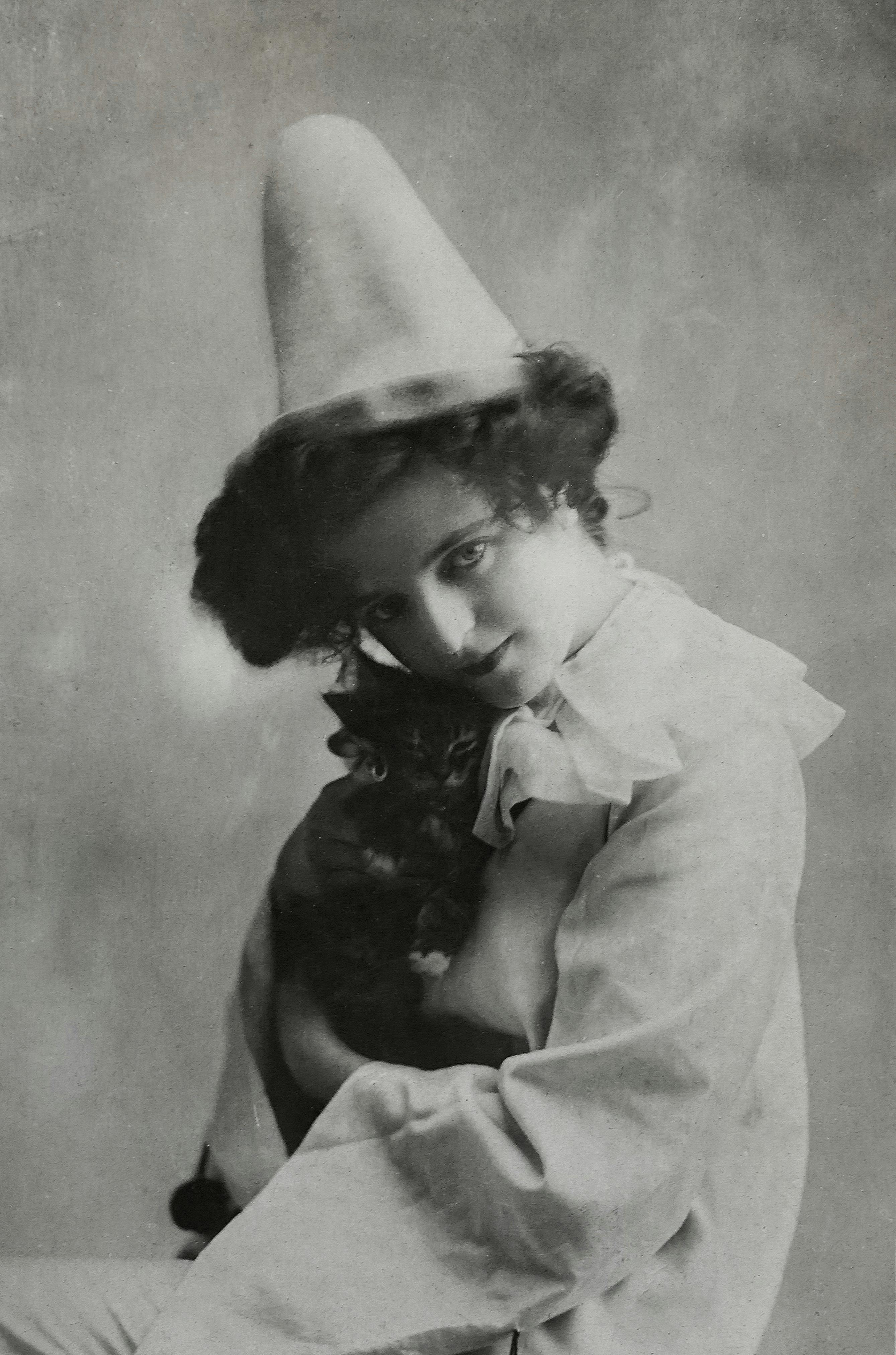 A black and white vintage portrait of a woman in a clown costume holding a cat.
