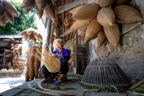 Free Elderly ethnic female working with timber fish traps near shabby brick house in yard Stock Photo
