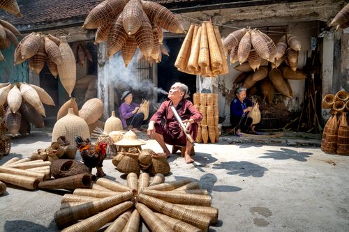 Free Elderly ethnic women making traditional Vietnamese wicker bamboo fish traps while aged man smoking near rural residential house Stock Photo