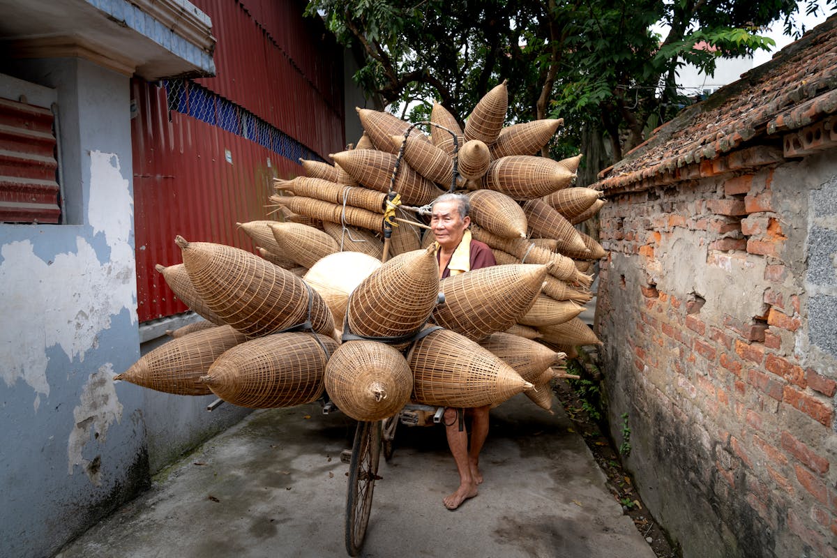Elderly Asian man carrying bamboo fish traps on street in poor district of village in daylight