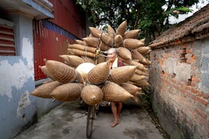 Elderly Asian man carrying bamboo fish traps on street in poor district of village in daylight
