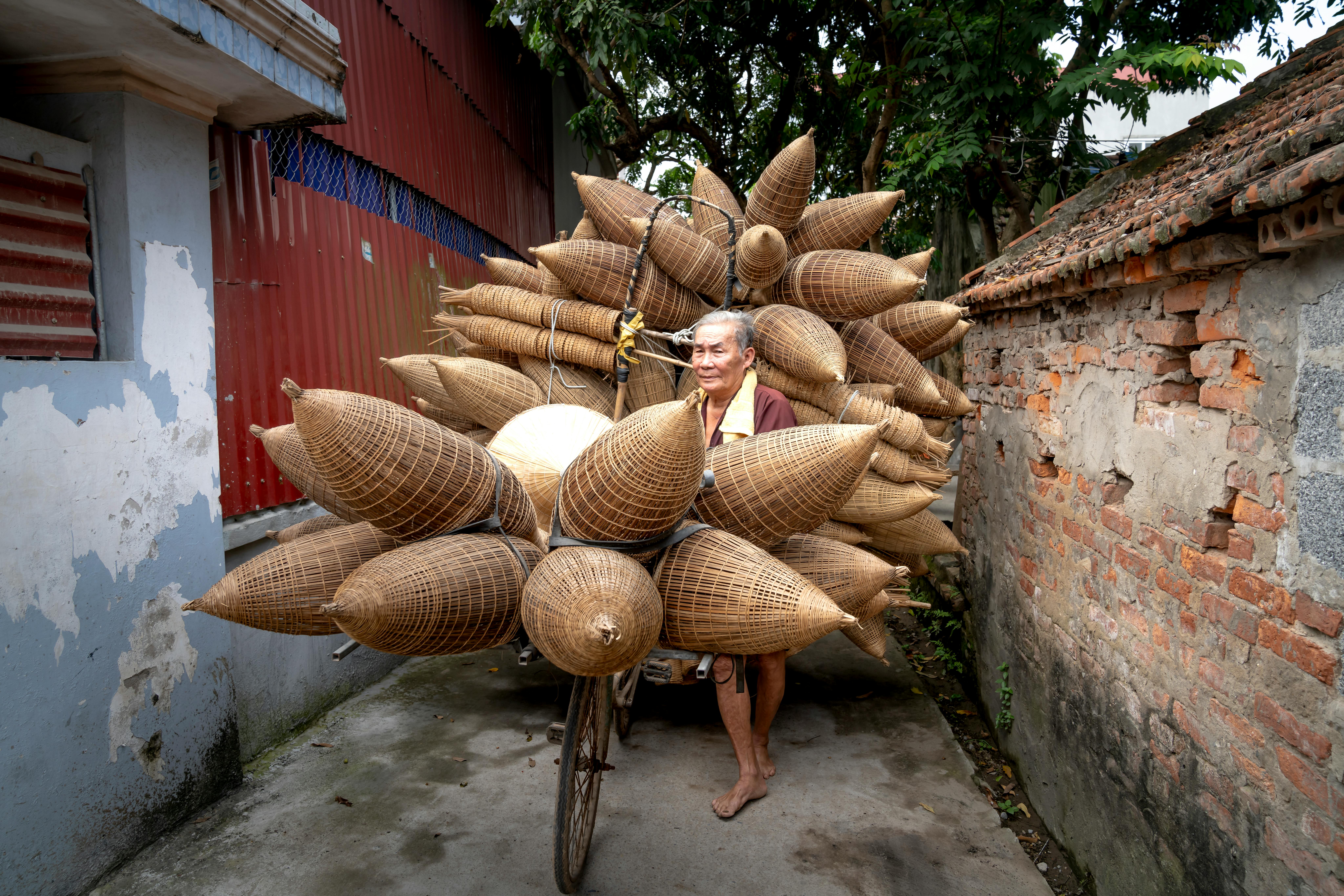 Asian man carrying bamboo fish traps in village in daylight · Free
