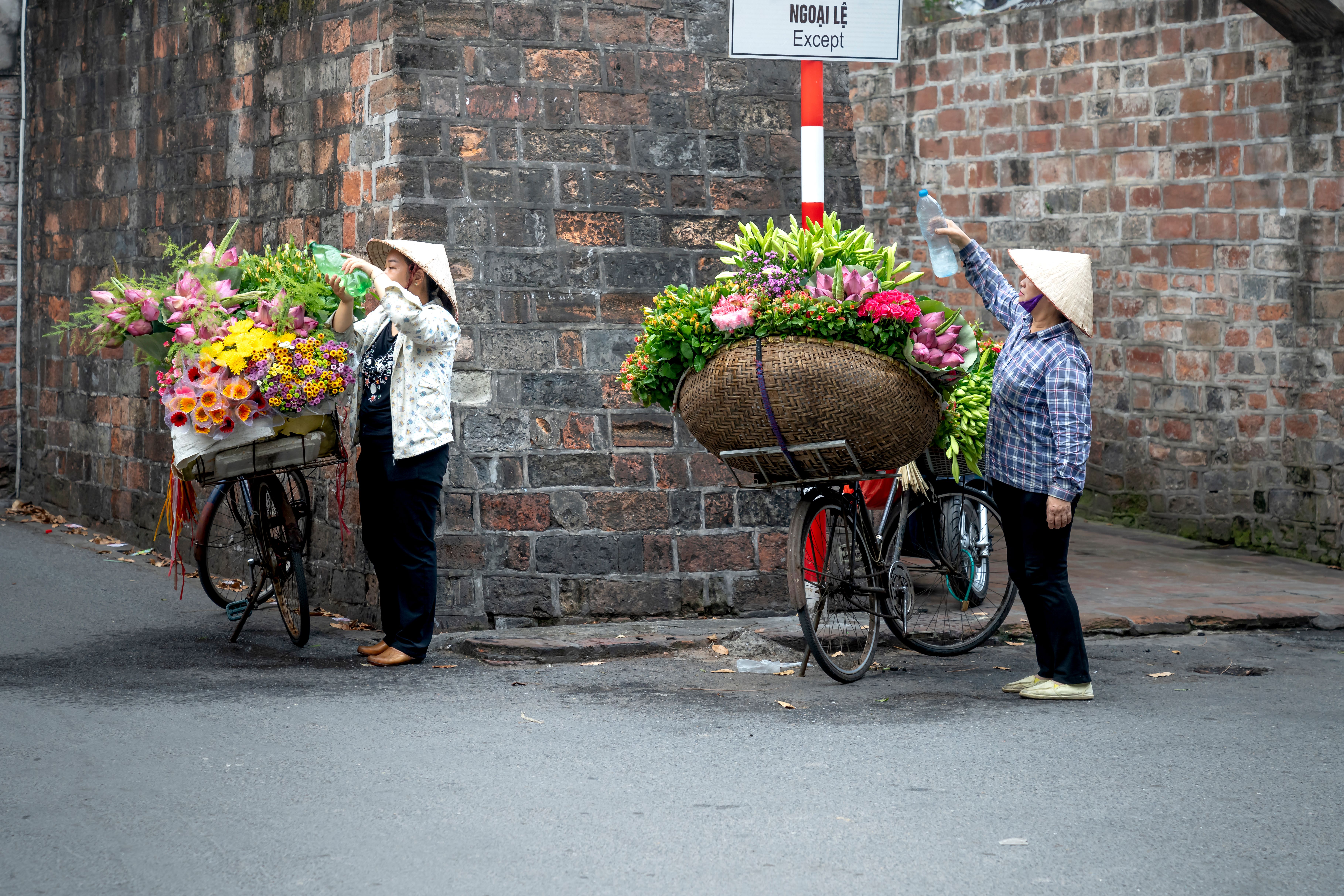 Two flower vendors with bicycles in Vietnam, selling colorful bouquets on a street.