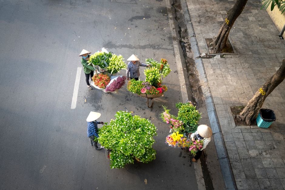 From above of unrecognizable people in Vietnam conical hats standing near bicycles with baskets of flowers for sale on street