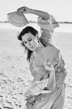 Graceful woman performing a fan dance on a beach in monochrome. Captivating and serene.