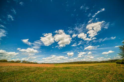 Free Expansive field with clouds floating in a bright blue sky, symbolizing tranquility and nature's beauty. Stock Photo