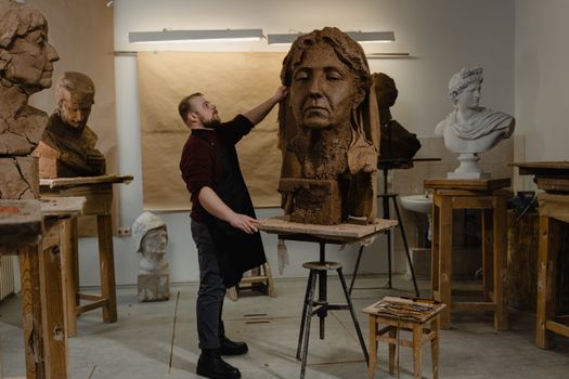 A male sculptor working diligently in an art studio, creating a large clay bust.