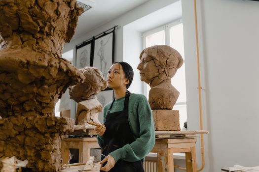 Woman sculptor working on clay busts in a well-lit art studio, showcasing craftsmanship.