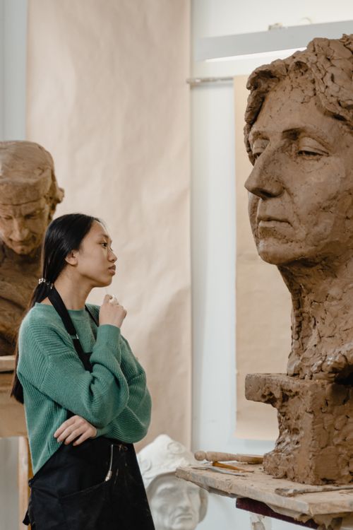 Free An artist in a green sweater examines a clay sculpture in an art studio, reflecting creativity. Stock Photo