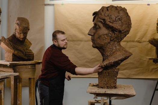 Focused sculptor modeling a clay bust in a creative art studio environment.
