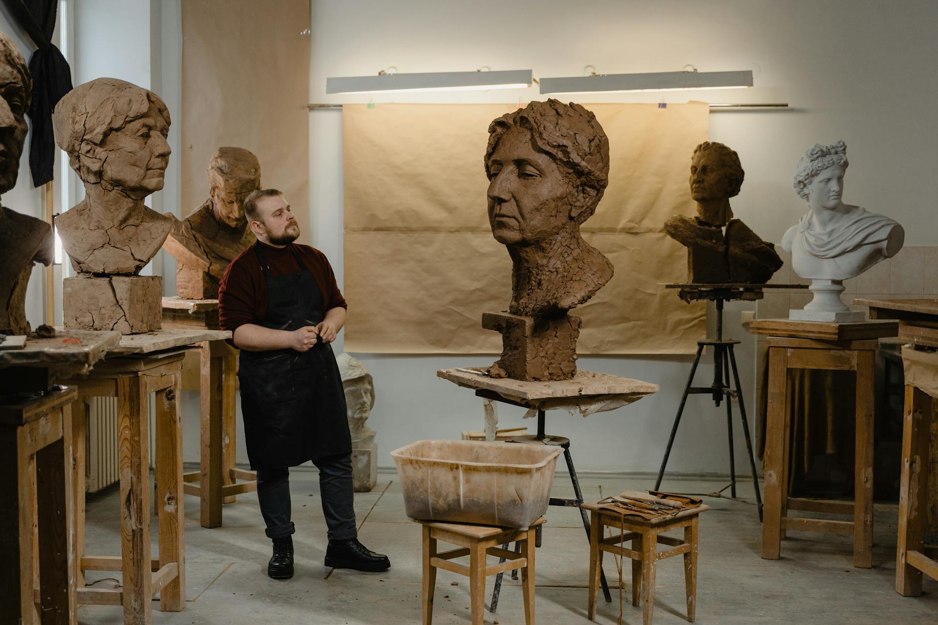 A sculptor in an art studio surrounded by clay busts demonstrates traditional craftsmanship.