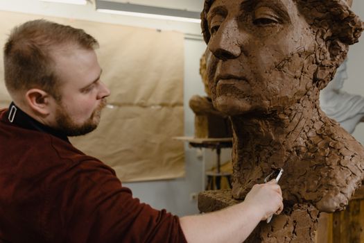 Artist focused on sculpting a detailed clay bust in a creative indoor art studio.