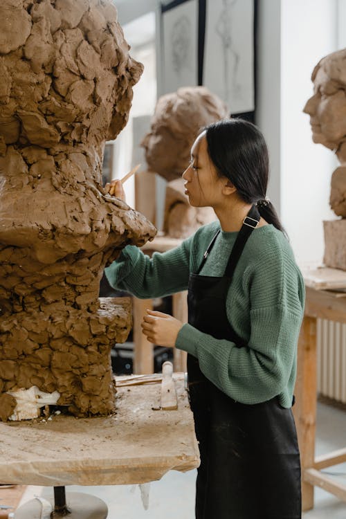 A Woman with Black Apron Carving a Clay
