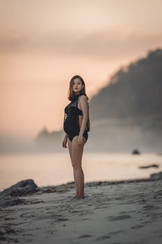 Serene image of a pregnant woman standing on a peaceful beach at sunset.