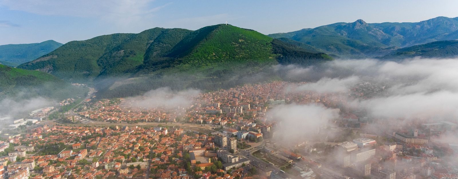 Scenic aerial view of a Bulgarian town surrounded by mist and lush green mountains.