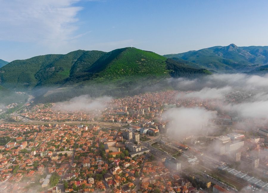 Scenic aerial view of a Bulgarian town surrounded by mist and lush green mountains.