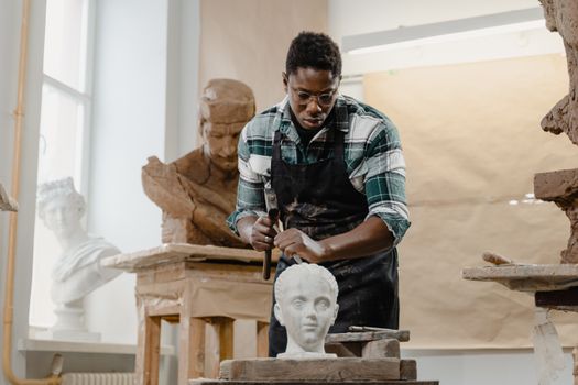 African American sculptor focused on shaping a clay bust in a bright, modern art studio.