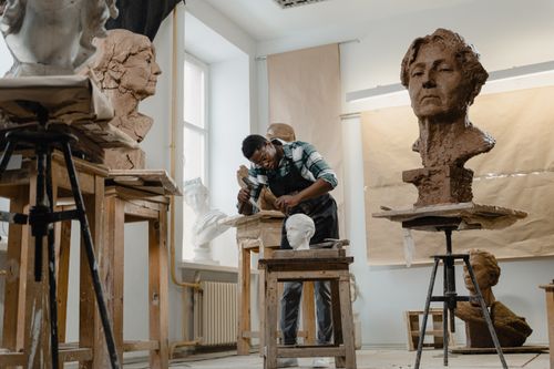 Free Artist working diligently on a clay sculpture in his art studio, surrounded by busts. Stock Photo
