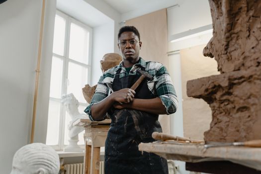 Talented African American sculptor in an art studio, holding tools for creative work.