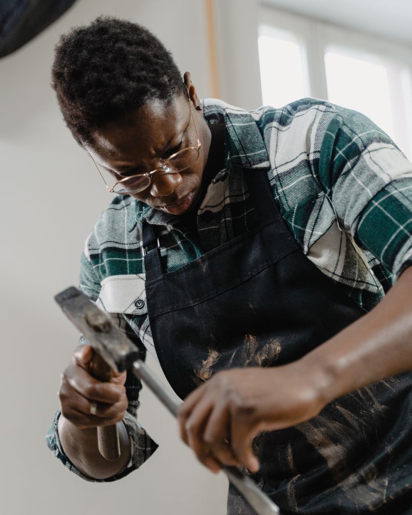 A sculptor in a work apron driving a chisel with a steel hammer into a pale carved block in a bright studio.