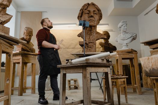 A sculptor working on a large clay bust in an artistic indoor workshop.