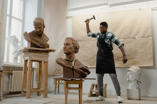 African American sculptor working with clay busts in art studio with hammer.