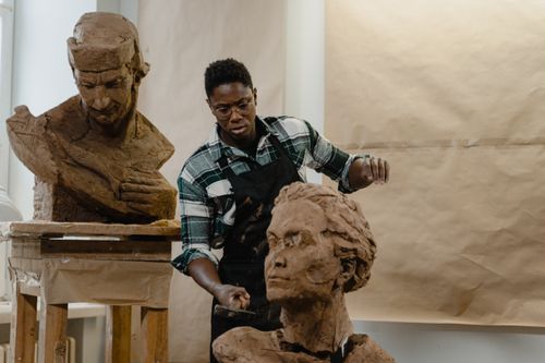 Free A sculptor skillfully works on clay busts in a bright art studio setting. Stock Photo