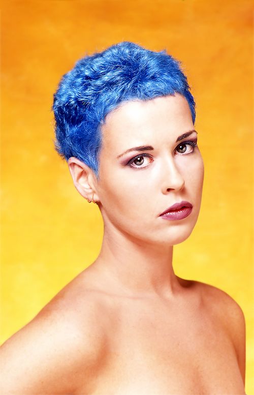 Free Studio portrait of a woman with striking blue hair on an orange background. Stock Photo