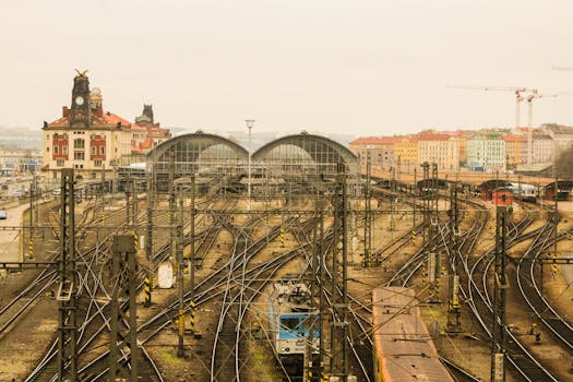 Railway tracks converging at Prague's historic train station under a cloudy sky.