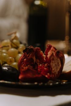 A close-up shot of fresh pomegranate, grapes, and pears on a dimly lit dining table.