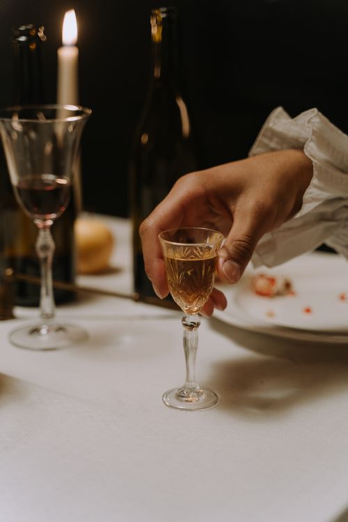 Free A close-up of a hand holding a wine glass on a candlelit dinner table, creating a cozy ambiance. Stock Photo