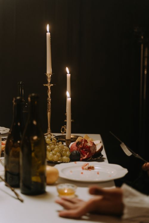 Free A moody candlelit dinner scene featuring wine bottles, fruits, and burning candles on a table. Stock Photo
