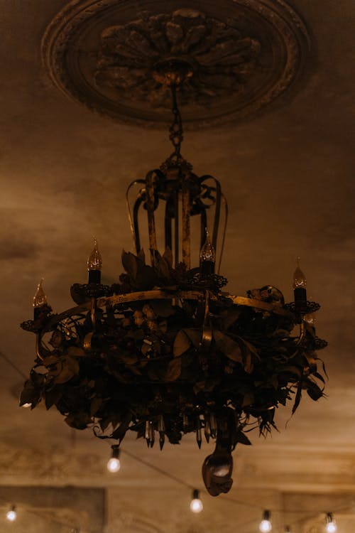 A Metal Chandelier Hanging from Ceiling Beside String of Light Bulbs