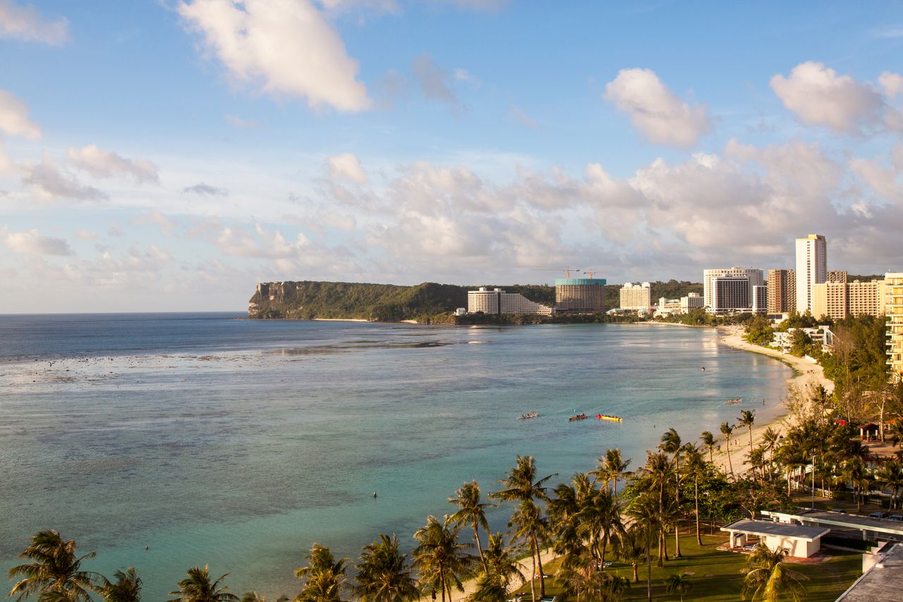 A beautiful aerial view of a tropical beach and cityscape in Guam, showcasing the coastline and modern architecture.