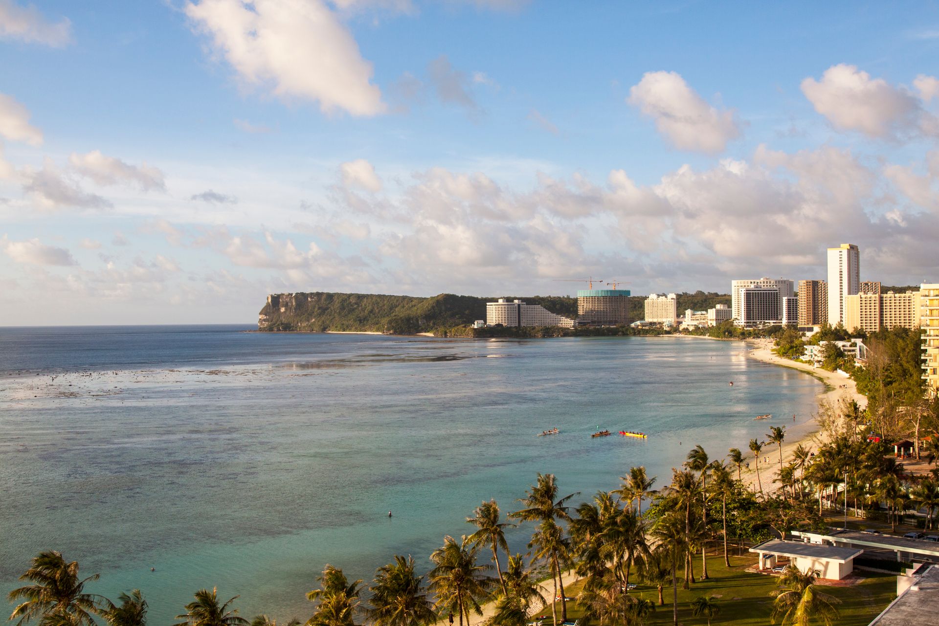 A beautiful aerial view of a tropical beach and cityscape in Guam, showcasing the coastline and modern architecture.