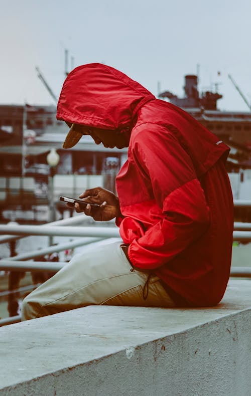A Man in a Red Jacket Looking at His Smartphone 