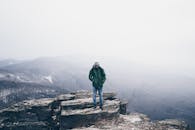 一名孤独的徒步旅行者站在岩石悬崖上，四周云雾缭绕，积雪累累